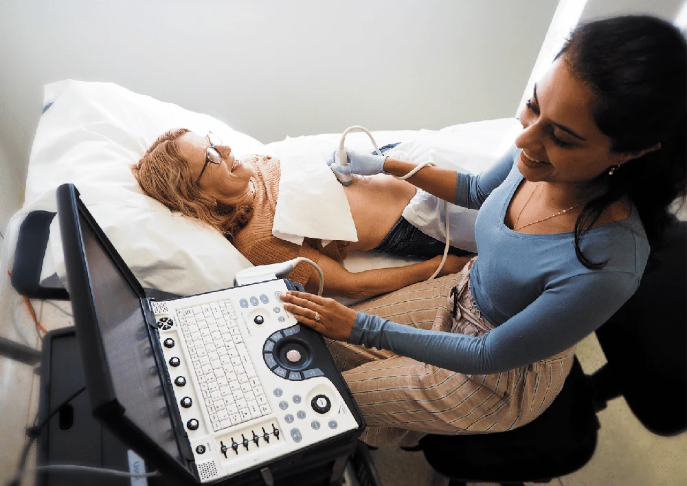 A sonographer performing a bedside ultrasound with portable equipment